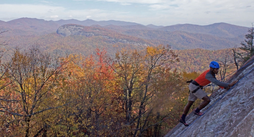 a person climbs a rock wall with fall foliage and a mountain landscape in the background